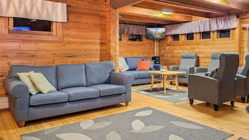 L’intérieur d’un chalet confortable, avec un canapé, des fauteuils, un téléviseur et une cheminée.