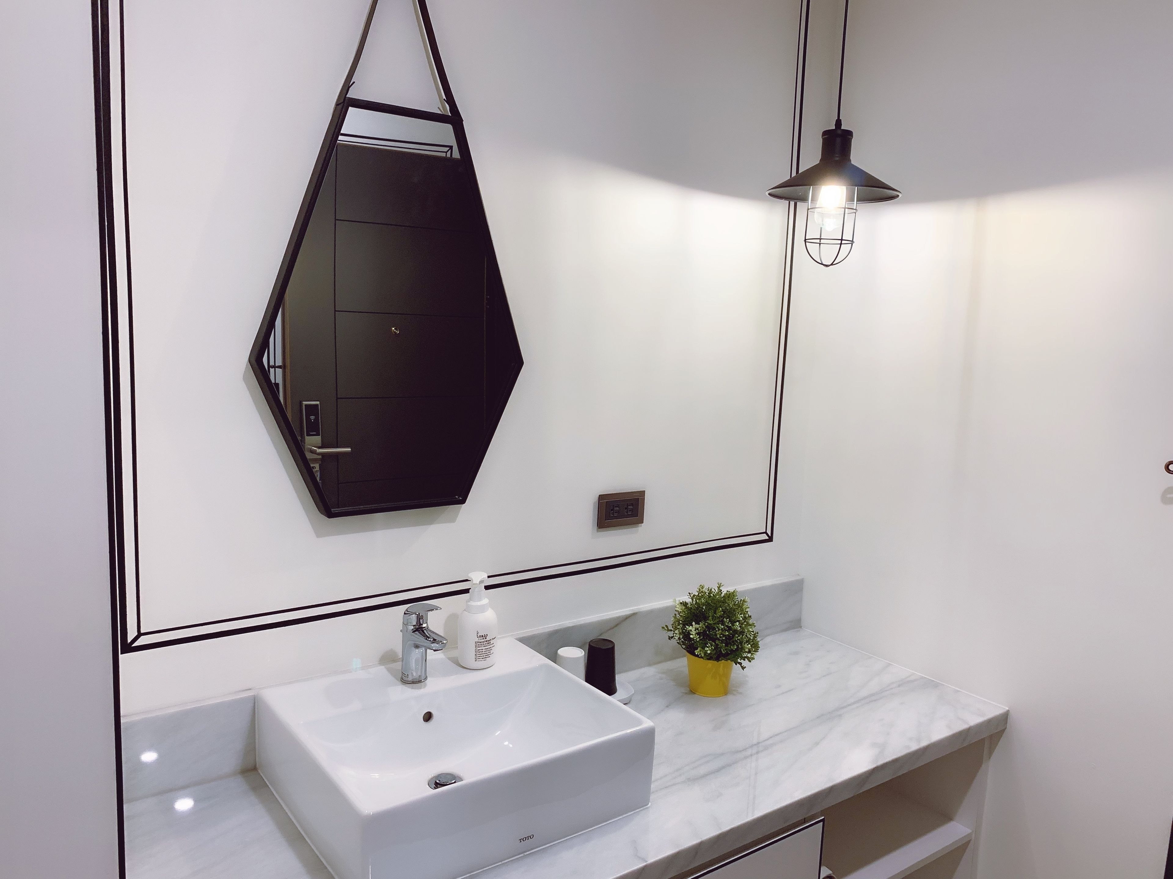 Un baño moderno con un lavamanos blanco, un espejo y una planta en maceta.