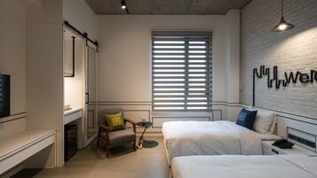A modern hotel room with two beds, a small seating area, a TV, and a large window with blinds.