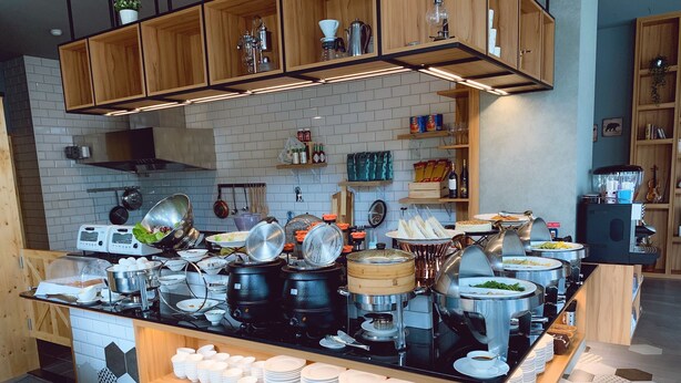 A buffet setup with various food items and condiments, a coffee machine, and stacked plates. - Tian Zhong Hotel (Tianzhong)