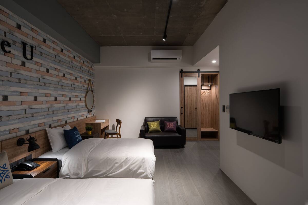Une chambre d’hôtel moderne avec un mur décoré d’un motif en briques, un téléviseur à écran plat, un canapé et un lit.