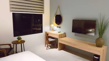 A modern bedroom with a bed, a desk with a chair, a TV, a small table with a plant, and a bench.