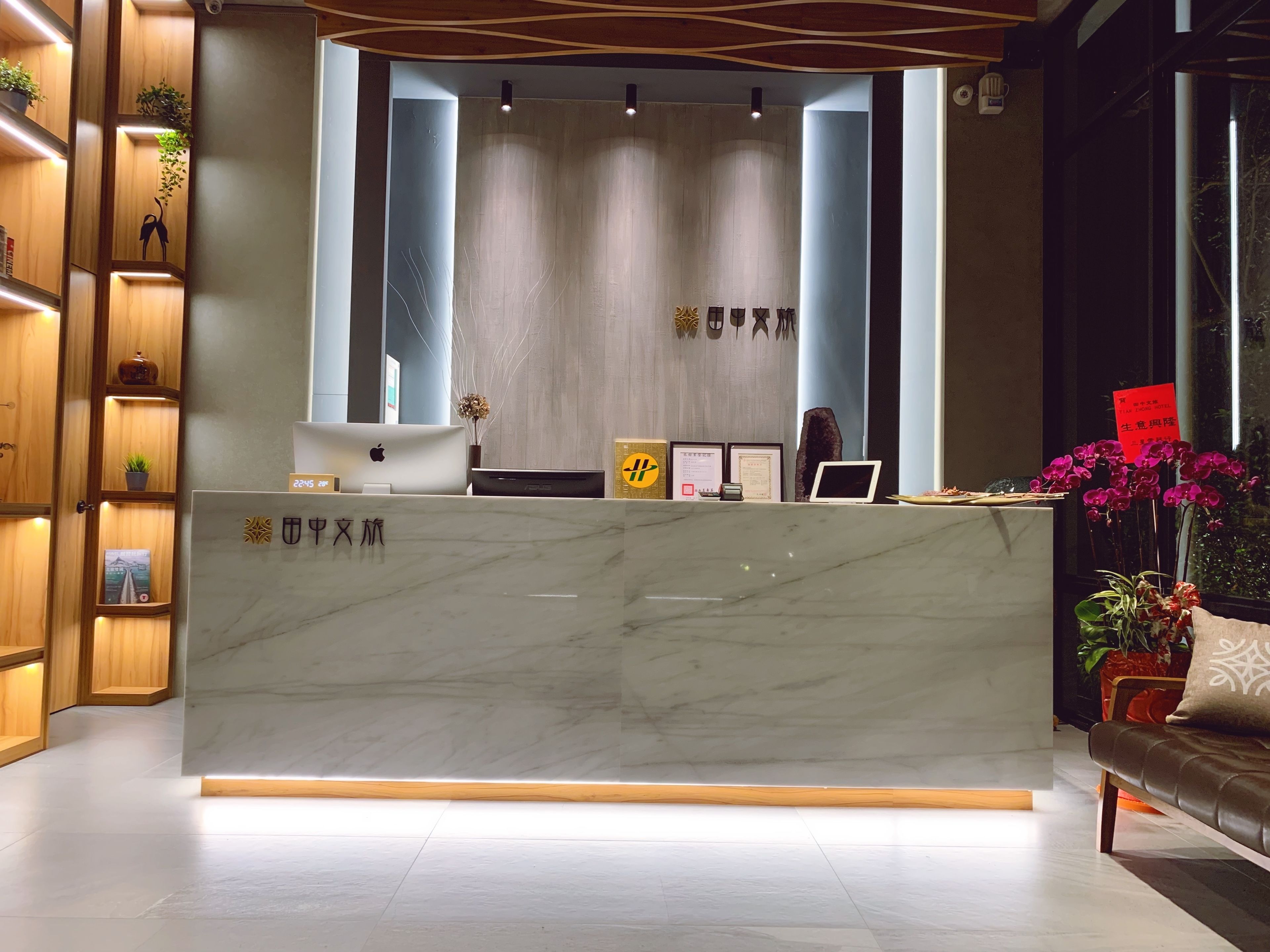 Una recepción con mostrador de mármol, estanterías de madera con plantas y un sofá con cojín.