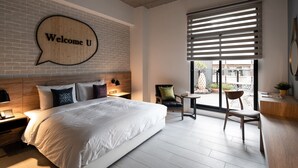 Une chambre d’hôtel moderne avec un grand lit, un panneau en bois en forme de bulle de dialogue, une petite table et une vue sur l’extérieur.