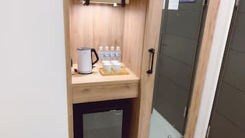 A compact kitchenette with a coffee maker, water bottles, and mugs on a wooden countertop.