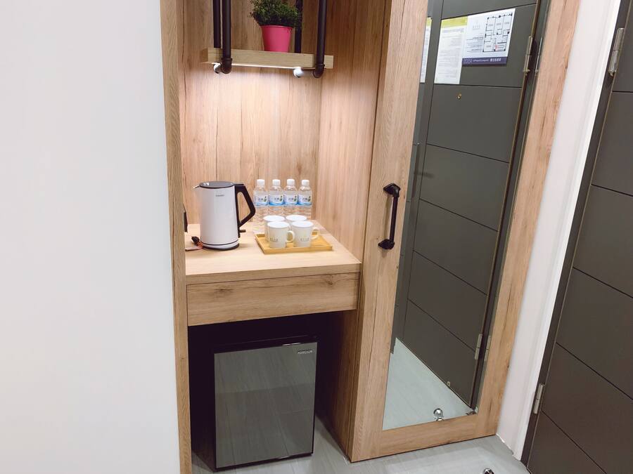 A compact kitchenette with a coffee maker, water bottles, and mugs on a wooden countertop.
