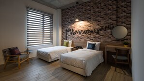 Une chambre moderne avec deux lits, un bureau et une chaise. Un mur en briques porte une inscription : « Bienvenue ».