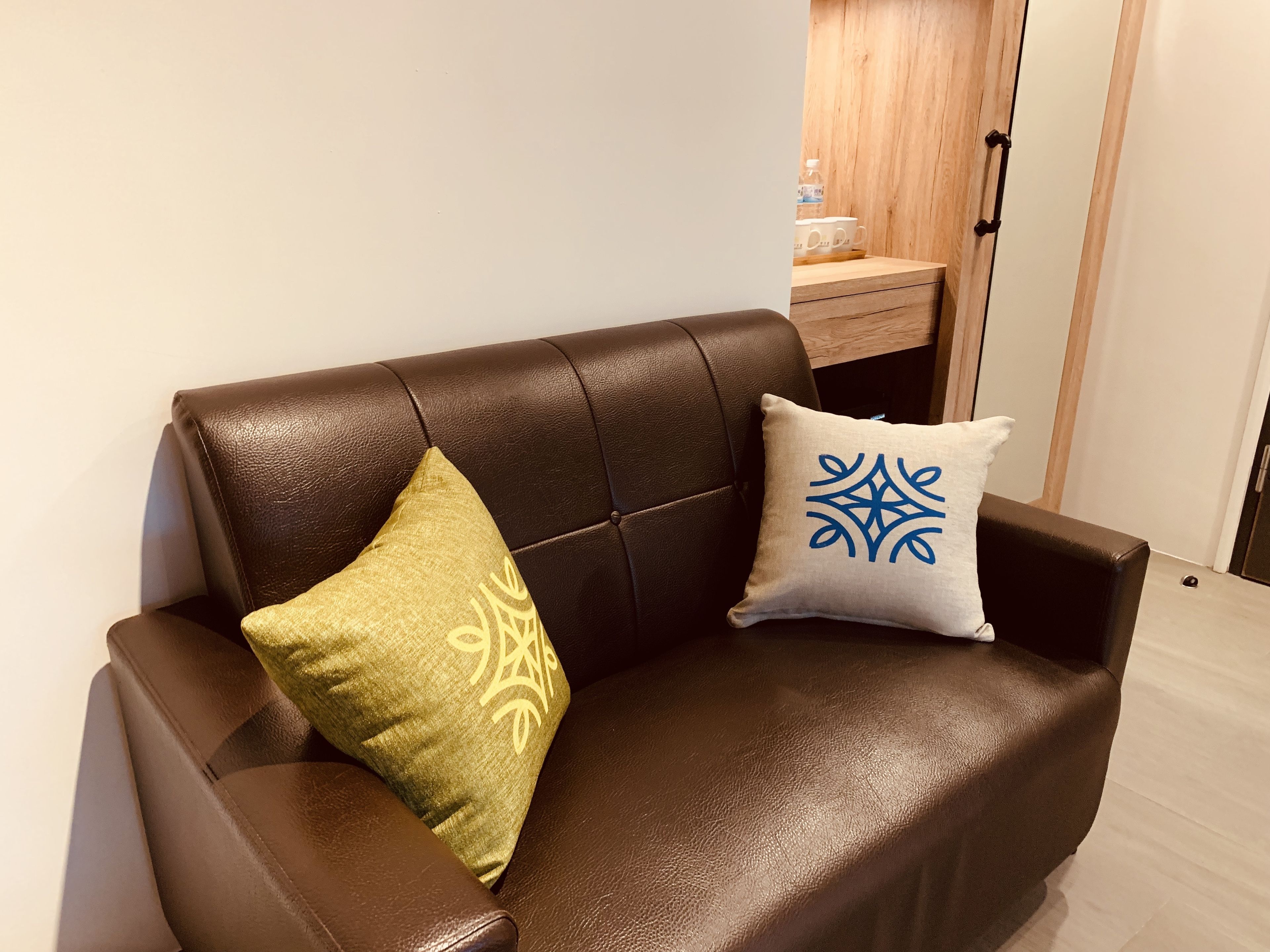 Un sofá de cuero marrón con dos cojines decorativos, una mesita de madera y una puerta de madera al fondo.