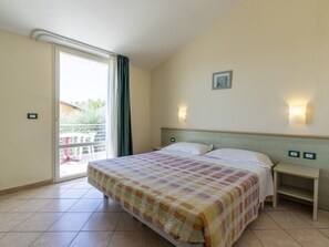 A hotel room with a bed, a nightstand, a wall-mounted light, and a sliding glass door leading to an outdoor area.