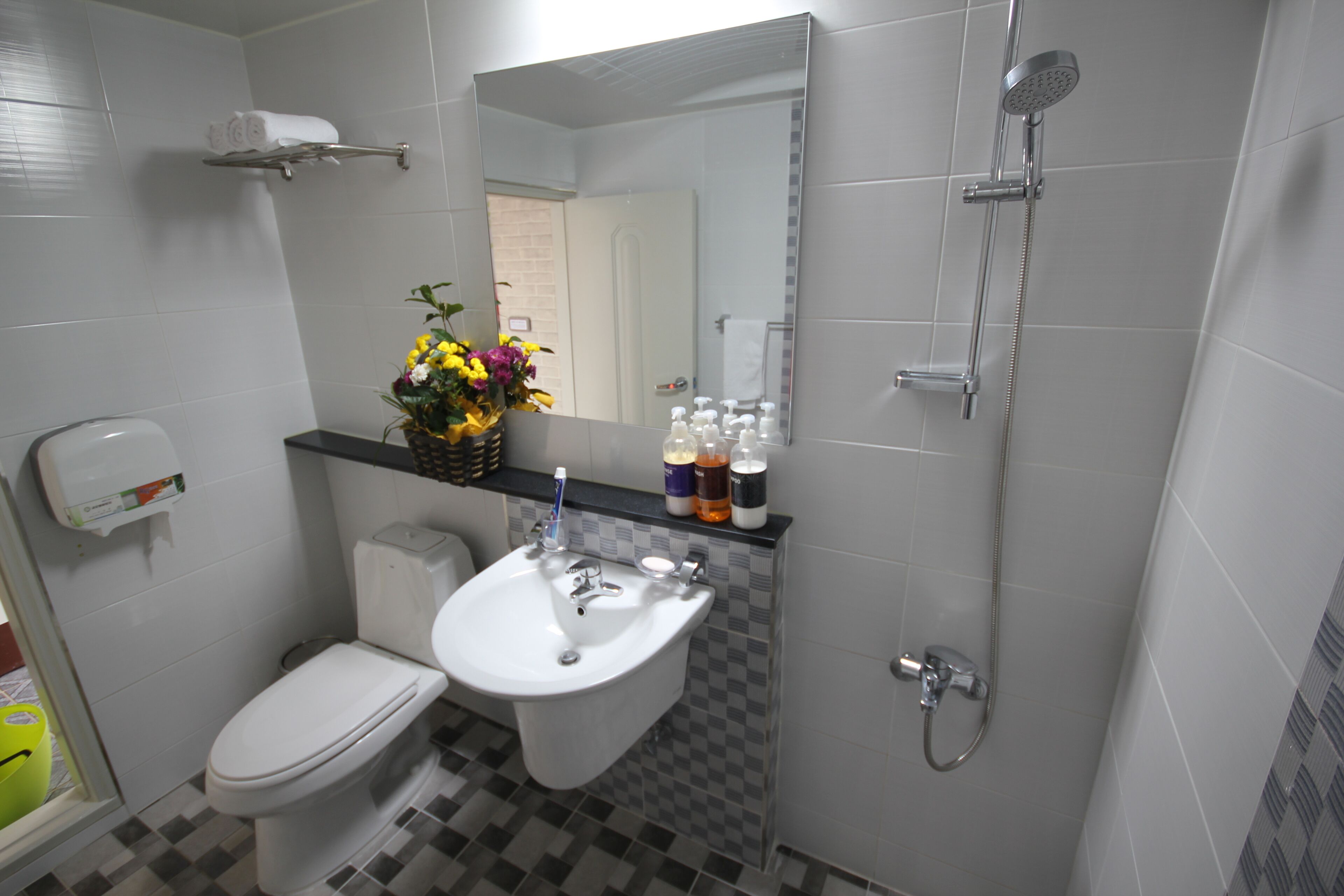 A bathroom with a toilet, sink, and shower. There is a mirror above the sink and a towel rack on the wall.