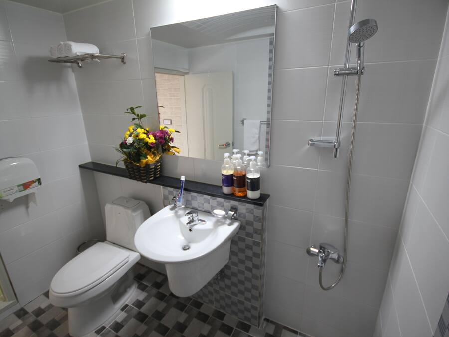 A bathroom with a toilet, sink, and shower. There is a mirror above the sink and a towel rack on the wall.