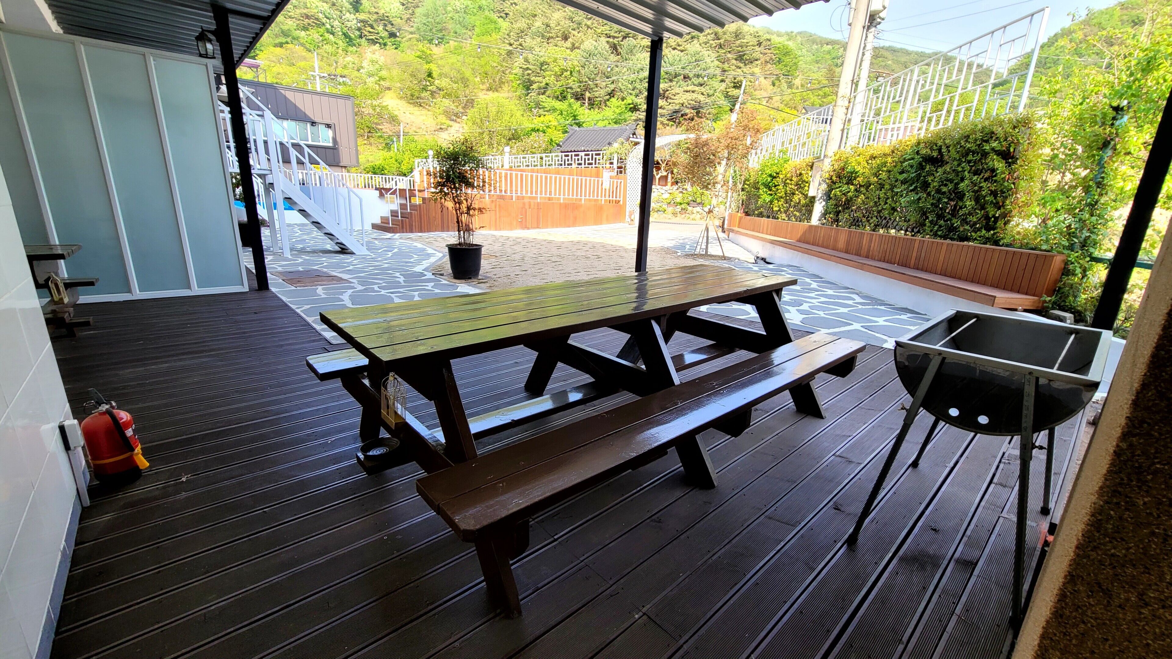 A covered outdoor area with a picnic table and grill, surrounded by a wooden deck and potted plants.