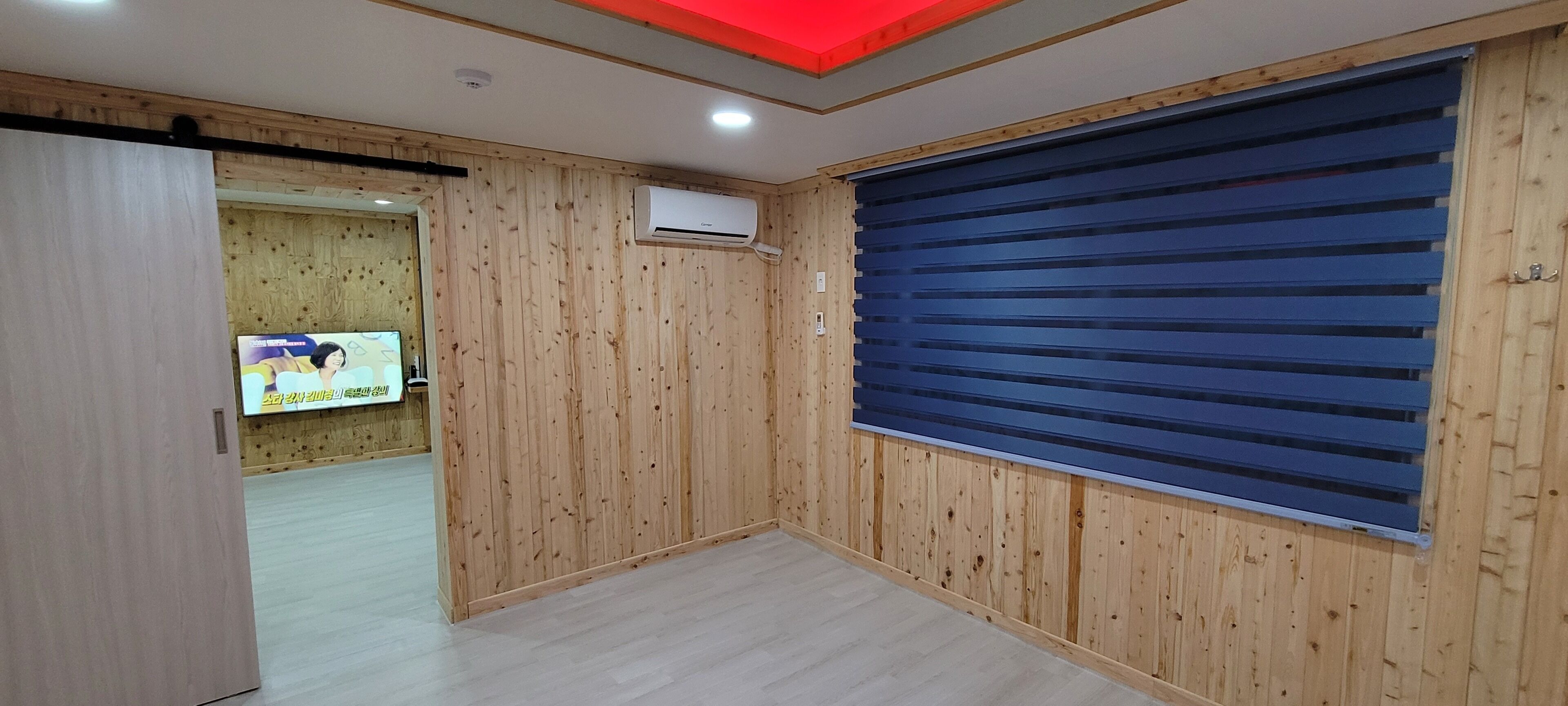 Una habitación con paredes de paneles de madera, una puerta azul con contraventanas cerradas y un equipo de aire acondicionado en la pared.