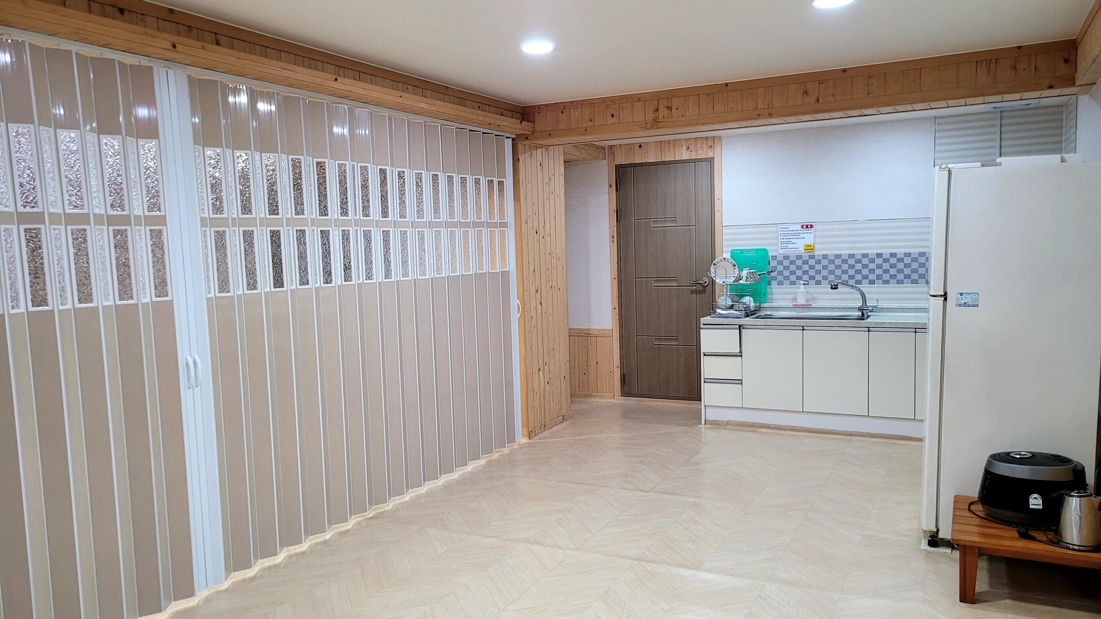 A kitchen with a wooden floor, white cabinets, a sink, and a refrigerator.
