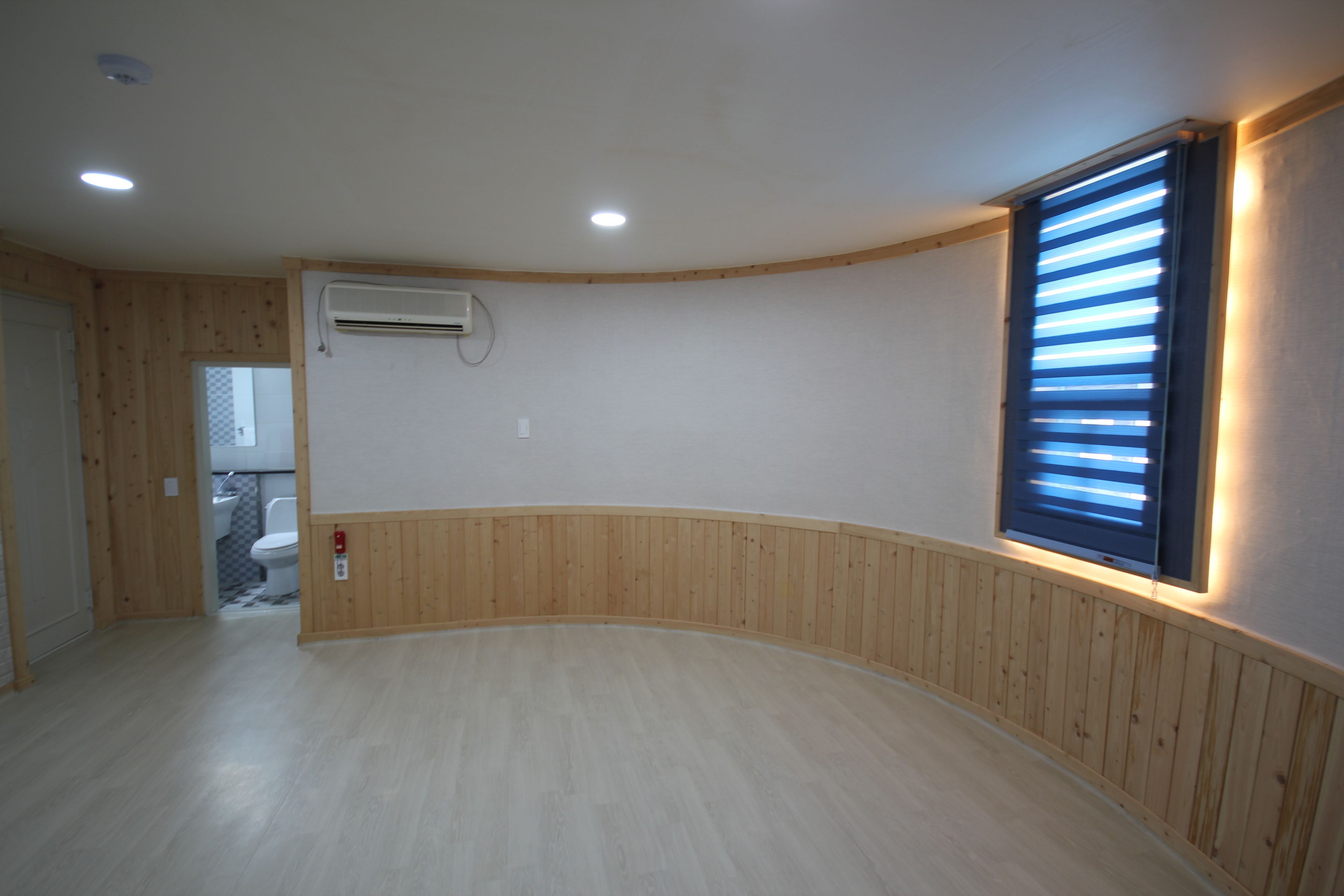 A room with wooden paneling, a white ceiling, and a window with horizontal blinds.