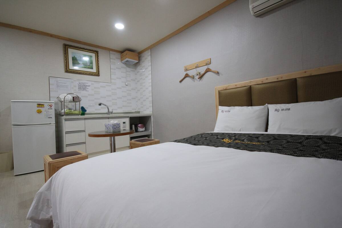 A hotel room with a bed, a small kitchenette, a refrigerator, a sink, and a wooden headboard.
