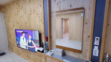 A room with wooden paneling, a television displaying a show, a mirror, and a small table with a phone and a box.