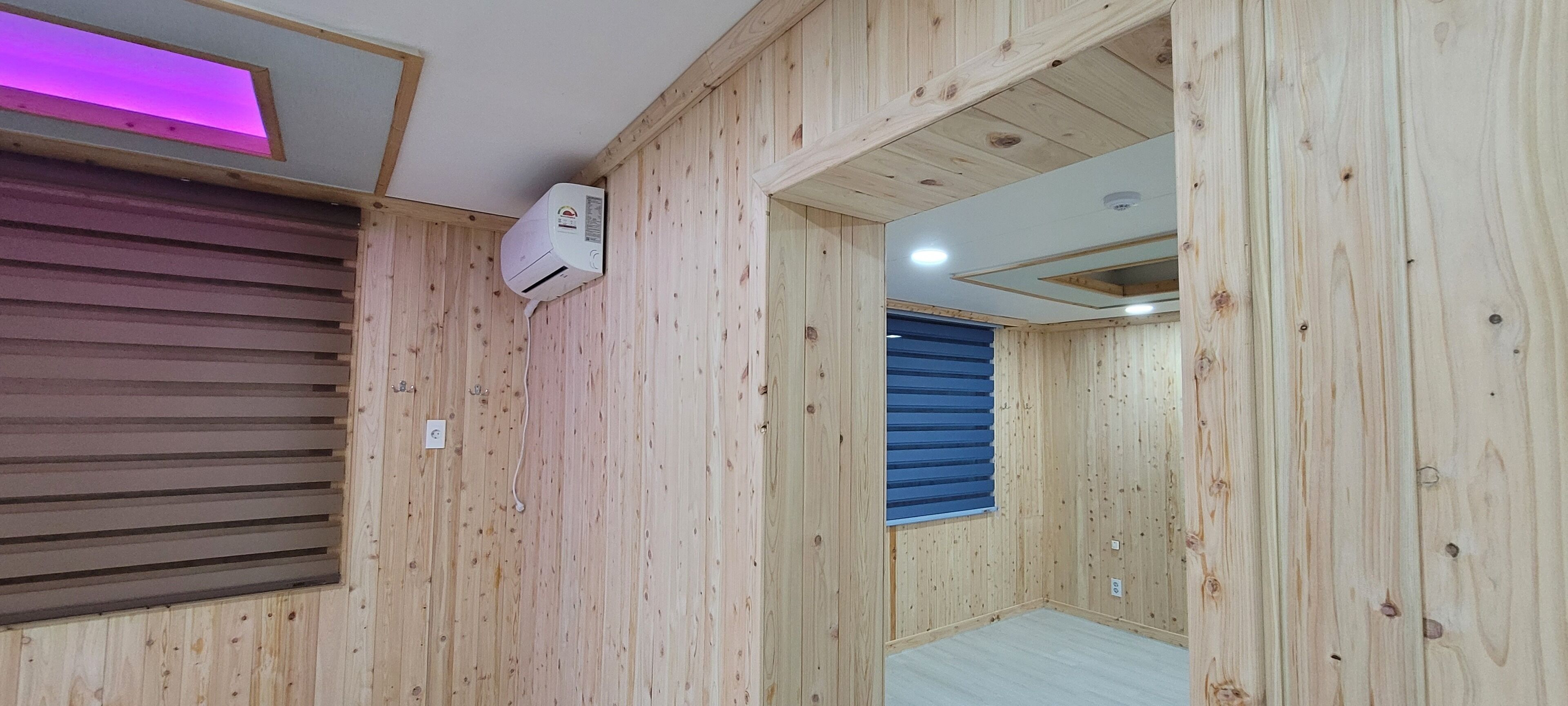 A room with wooden walls, a ceiling fan, and a window with blinds.