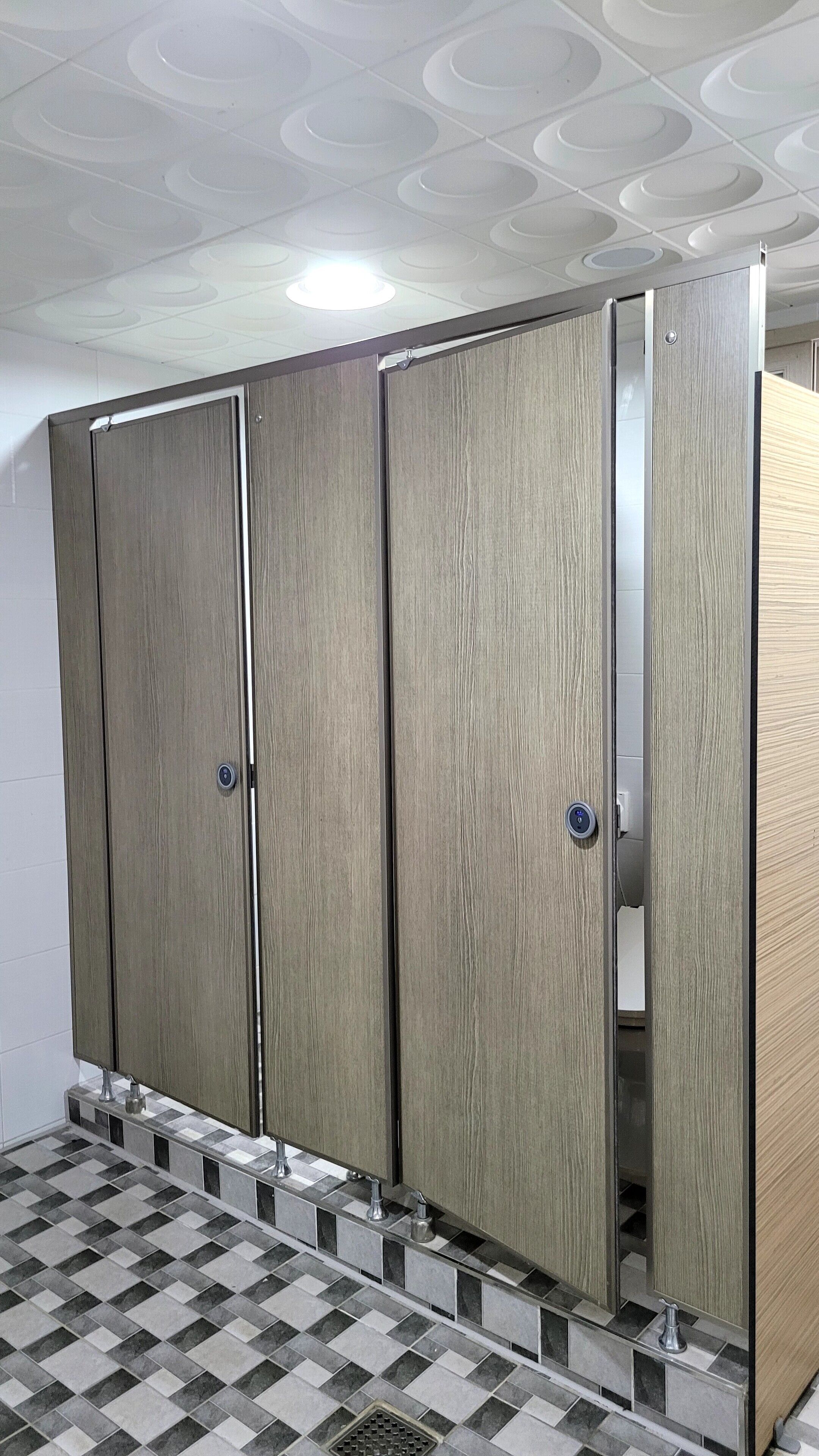 Des toilettes avec des casiers en bois, un sol carrelé et un plafond doté d’un éclairage encastré.
