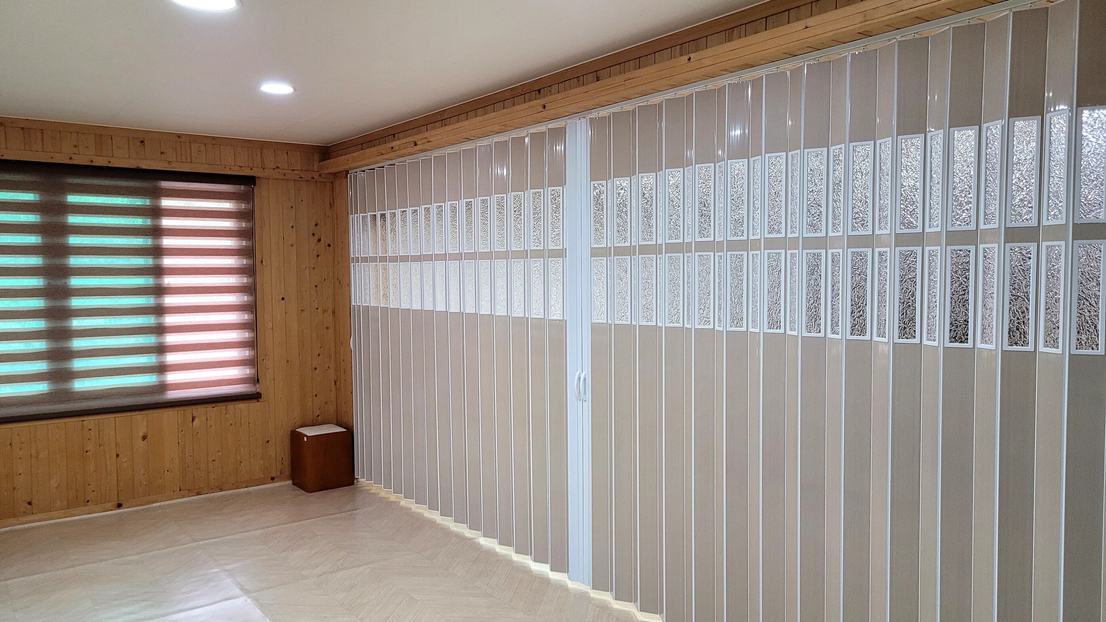 Une pièce avec des lambris en bois, une grande fenêtre avec des stores et un panneau décoratif au mur.