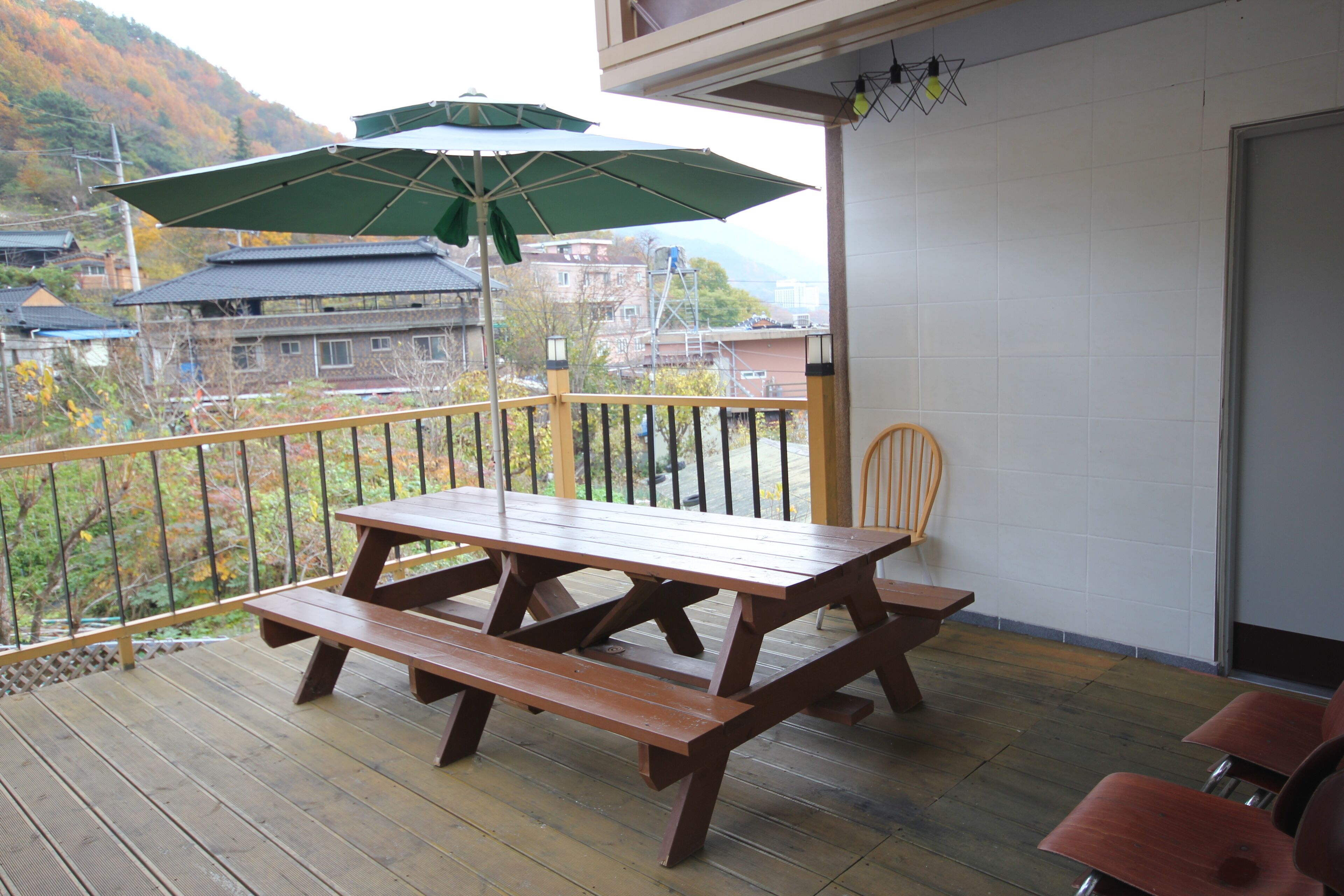 Um deck de madeira com mesa de piquenique e bancos, uma cadeira e um guarda-sol verde.