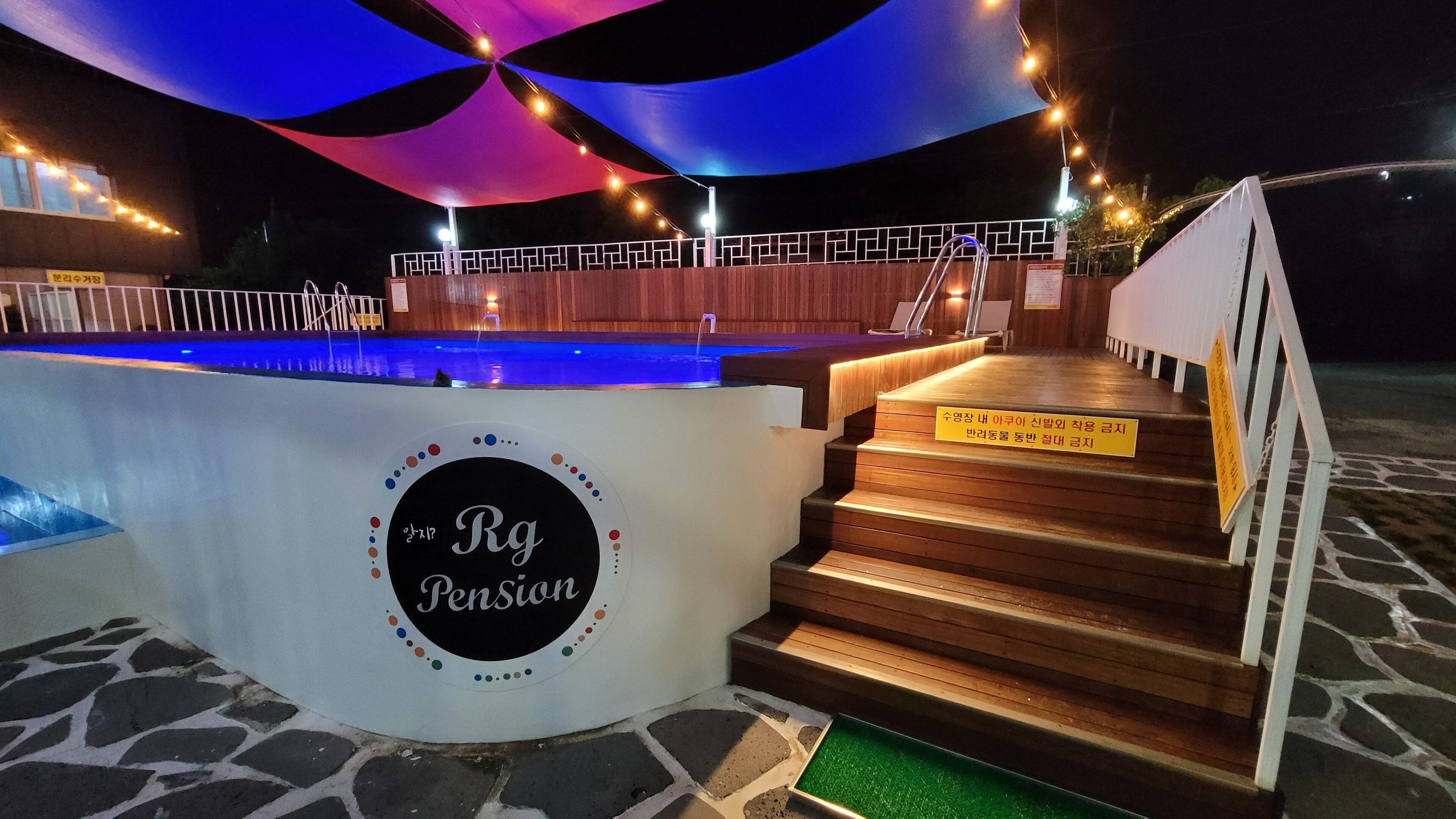 Un área de piscina con un cartel que dice "Rg Pension" y una escalera que sube a una terraza de madera.