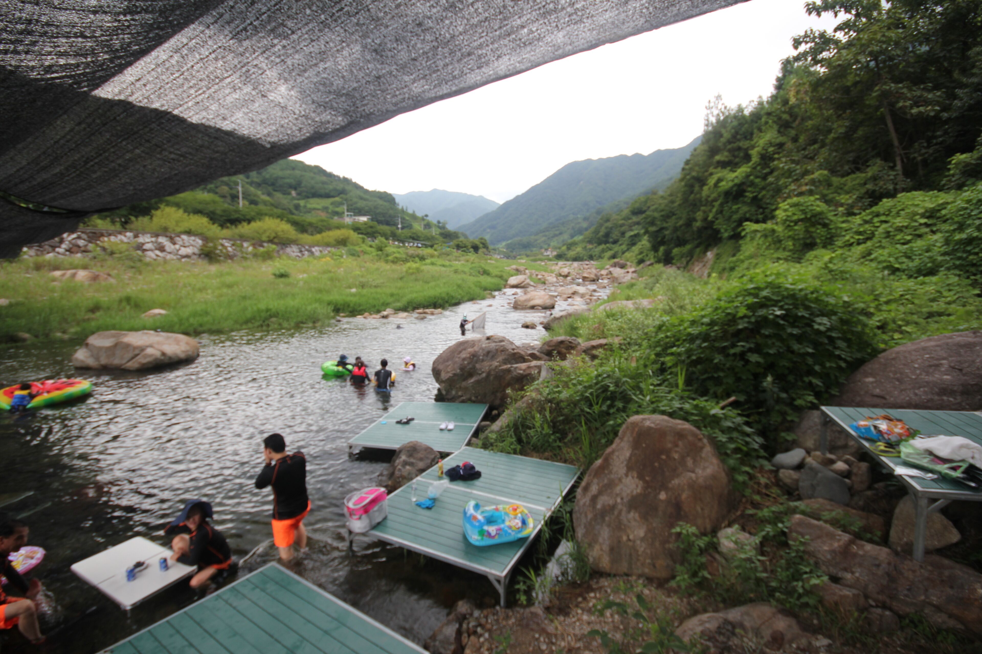 A riverside area with a bridge, boats, and people.