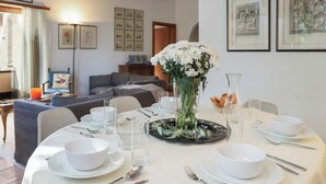 A dining table set with white plates, bowls, and cutlery, a vase with white flowers, and a glass pitcher.