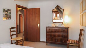 A hotel room with a bed, a wooden dresser, two chairs, a mirror, and a wall-mounted light.