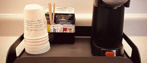 Una bandeja con una cafetera, una pila de tazas blancas y una caja de cigarrillos Big Flow.