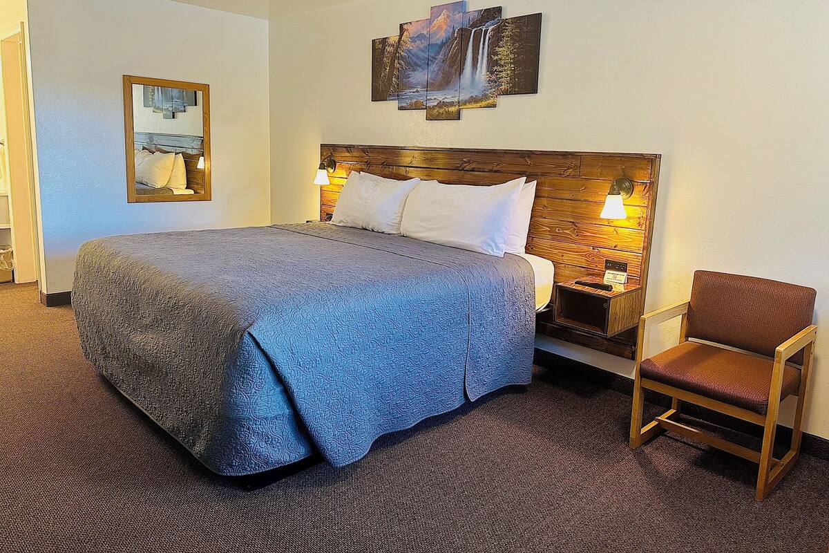A hotel room with a large bed, a wooden headboard, two bedside lamps, a chair, and a painting on the wall.