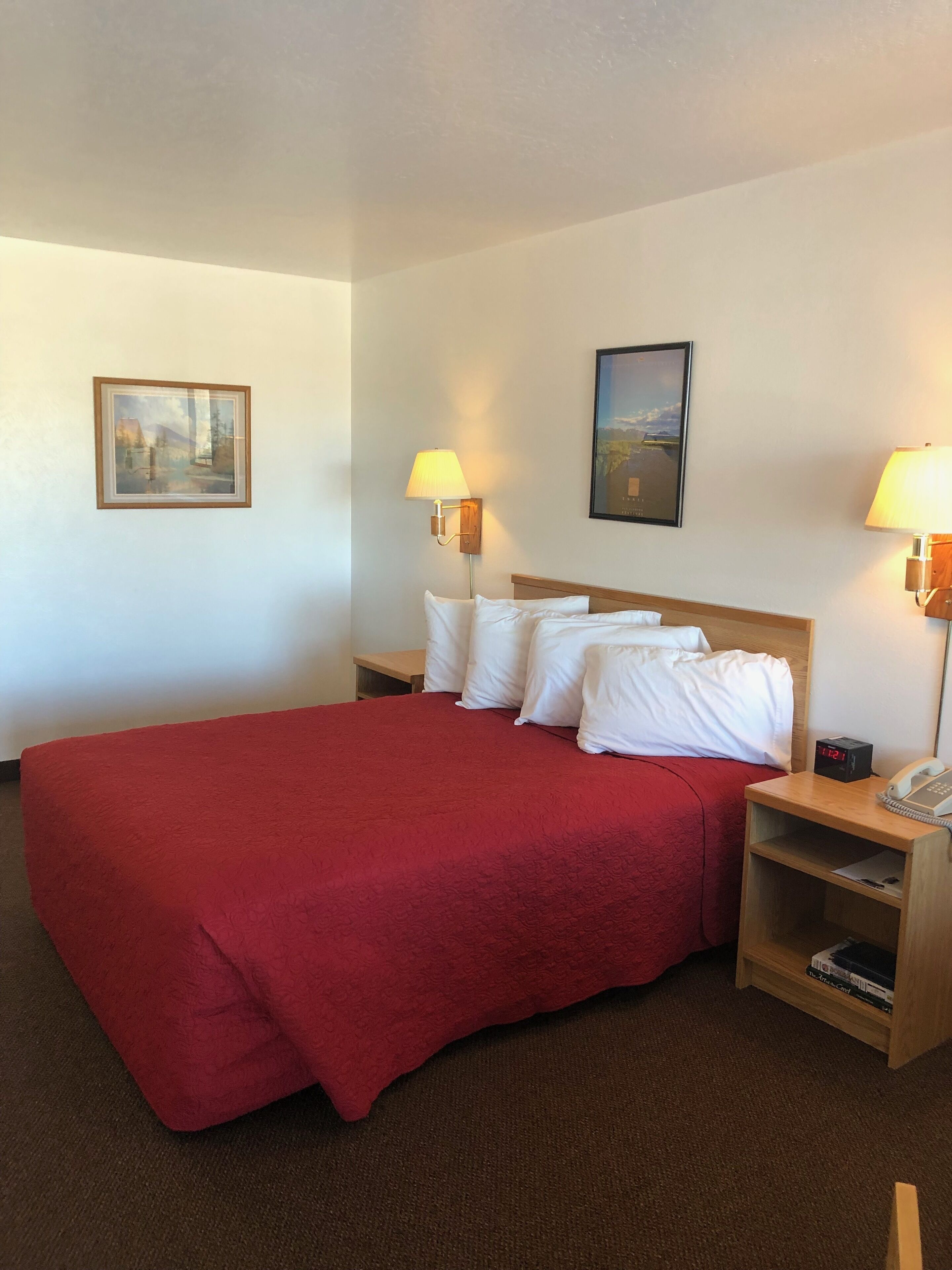 Une chambre d’hôtel avec un grand lit, deux tables de chevet, une petite table, une lampe fixée au mur et un tableau encadré accroché au mur.