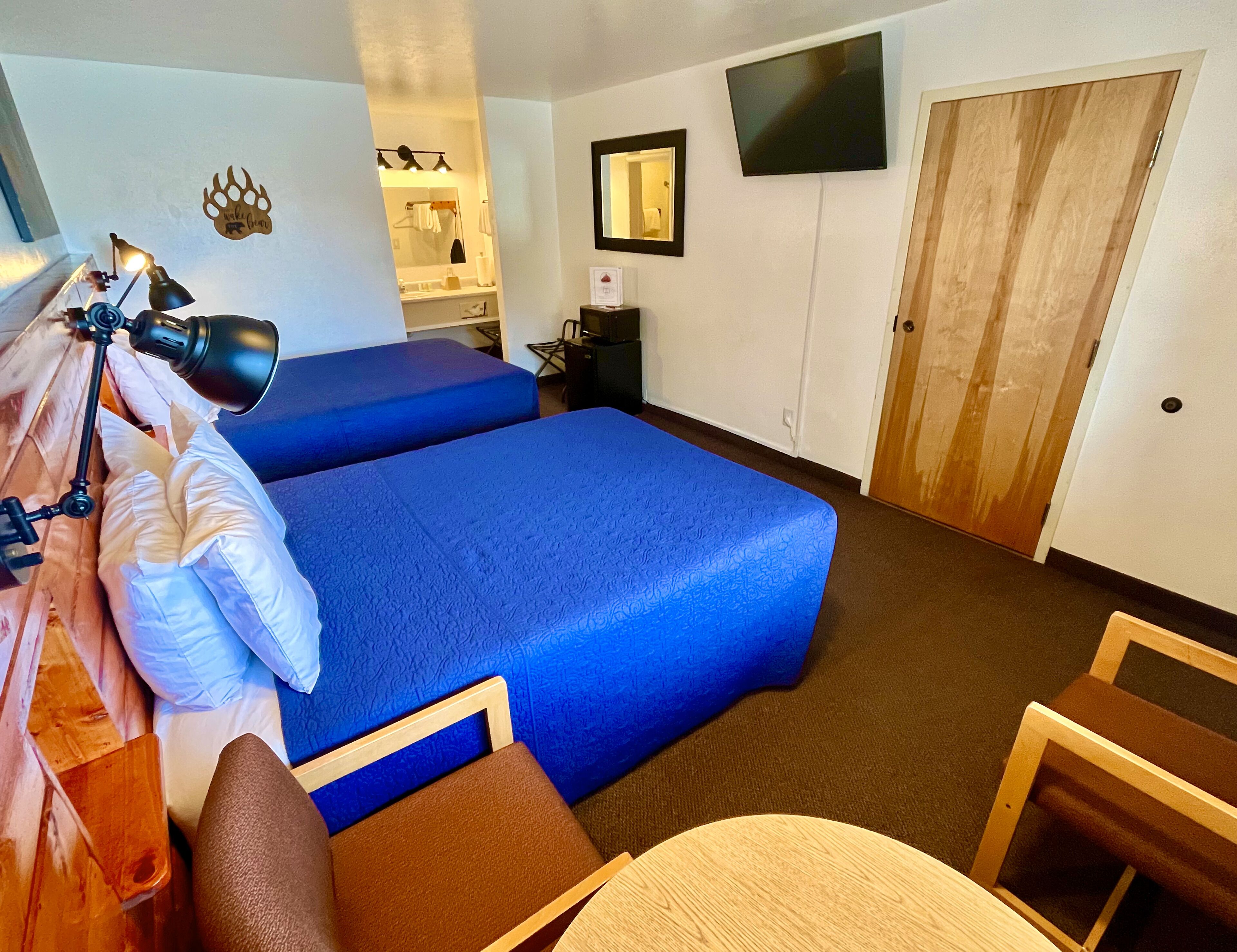 Une chambre d’hôtel avec deux lits, un bureau avec une lampe, un miroir, une télévision et une armoire.