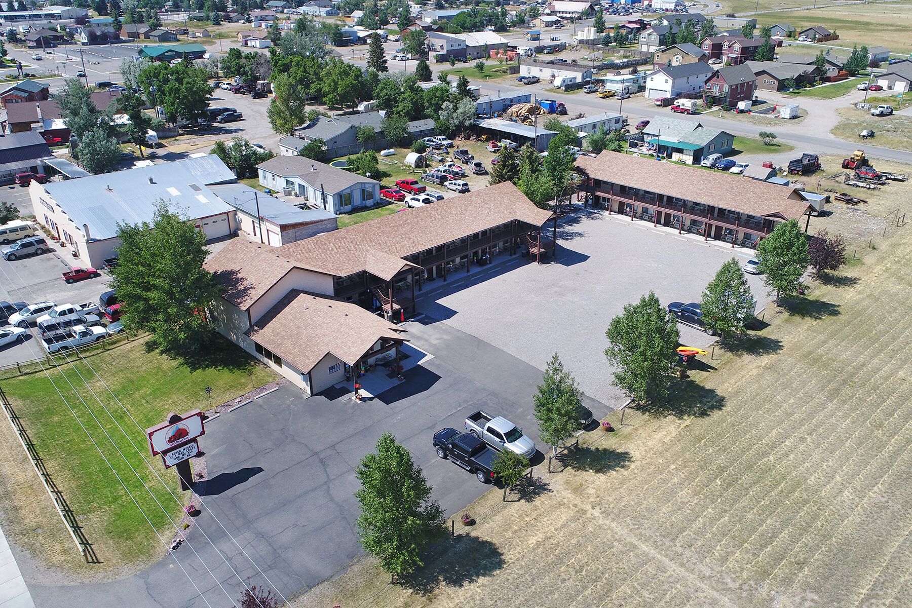 An aerial view of a commercial building with a large parking lot, surrounded by residential houses and greenery.