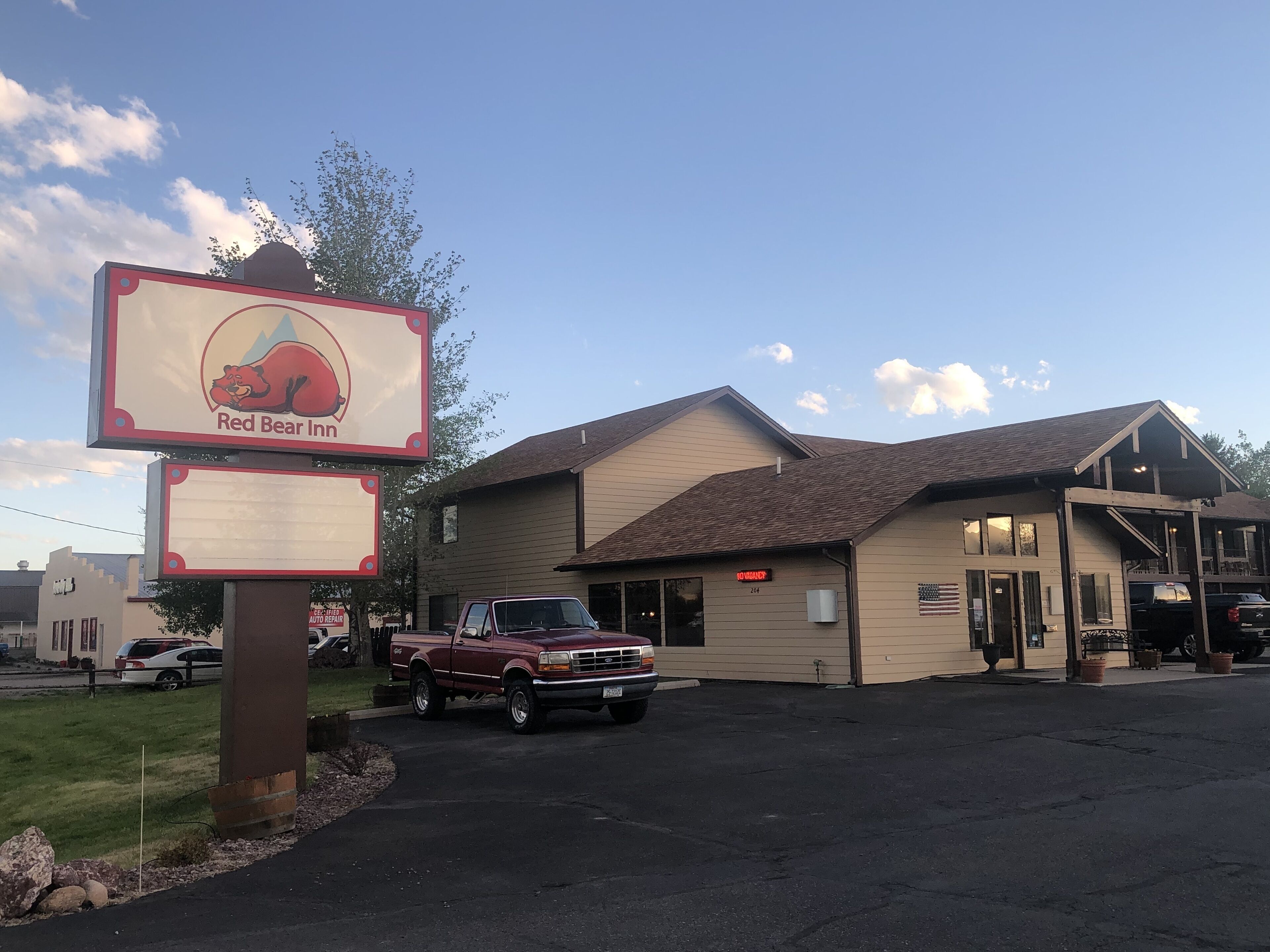 A Red Bear Inn with a parking lot, a red pickup truck, and a building with a brown roof.