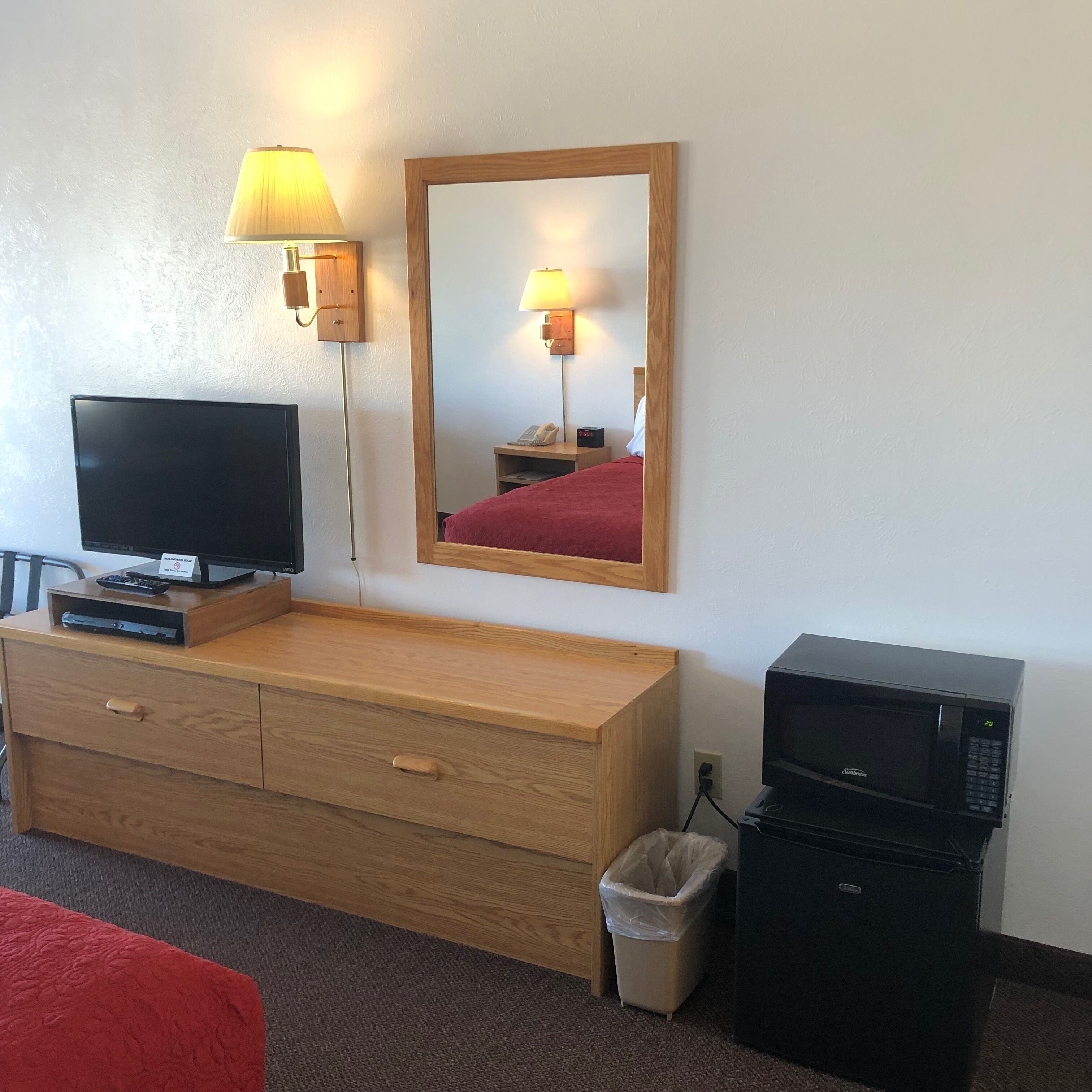 Hotellihuone, jossa on puinen lipasto, televisio, peili, lamppu, mikroaaltouuni ja roskakori.