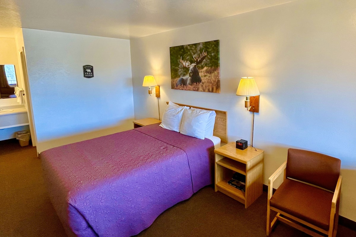 A hotel room with a large bed, two bedside tables with lamps, a chair, and a painting on the wall.