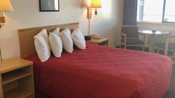 Ein Hotelzimmer mit einem großen Bett, zwei Nachttischen, einem Schreibtisch mit Stuhl, einem Fenster mit Vorhängen und einer Wandlampe.