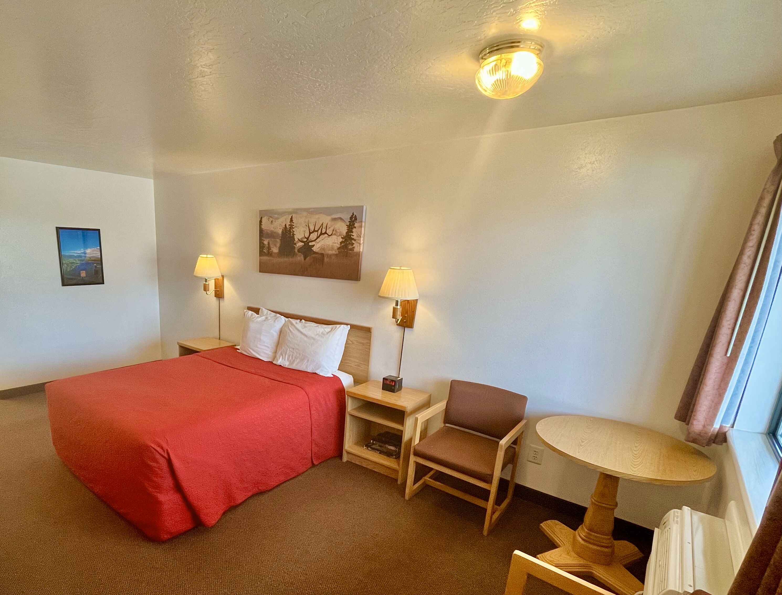 A hotel room with a large bed, two bedside lamps, a chair, a small table, and a painting on the wall.