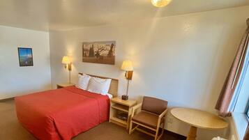A hotel room with a large bed, two bedside lamps, a chair, a small table, and a painting on the wall.