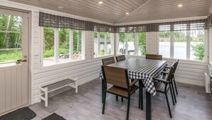 A covered dining area with a table set for six, surrounded by large windows offering a view of the outdoors.