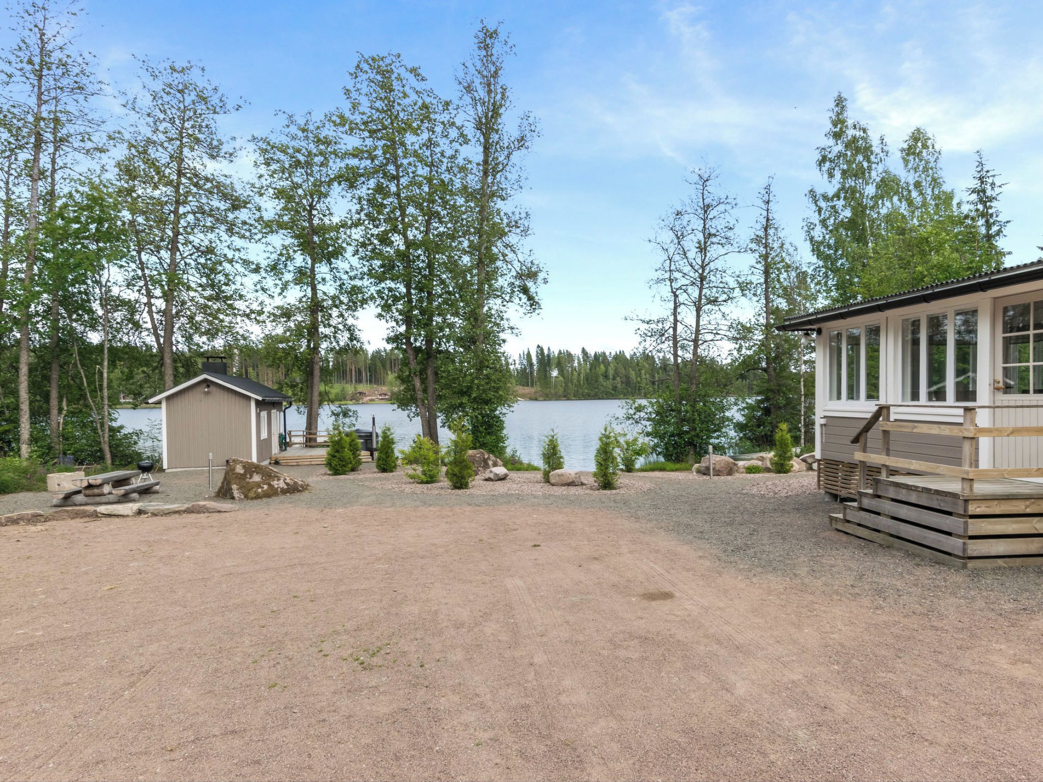 A lakeside cabin with a deck, a small shed, and a gravel area.