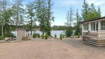 A lakeside cabin with a deck, a small shed, and a gravel area.