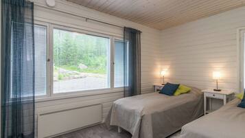 Une chambre avec deux lits, une fenêtre avec des stores, un luminaire au plafond et une table de chevet avec une lampe.