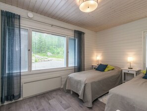 Een slaapkamer met twee bedden, een raam met luxaflex, een plafondlamp en een nachtkastje met een lamp.