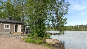 A cabin with a dock extending into a lake, surrounded by trees and a gravel path.