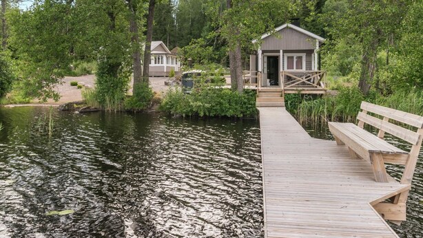 A wooden dock leading to a cabin with a porch, surrounded by dense trees and a calm lake.