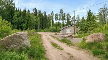Eine kleine Holzhütte mit einem Feldweg, der davor hindurchführt, umgeben von Bäumen und Steinen.