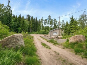 Een klein vakantiehuisje met een onverharde pad er naartoe, omringd door bomen en rotsen.