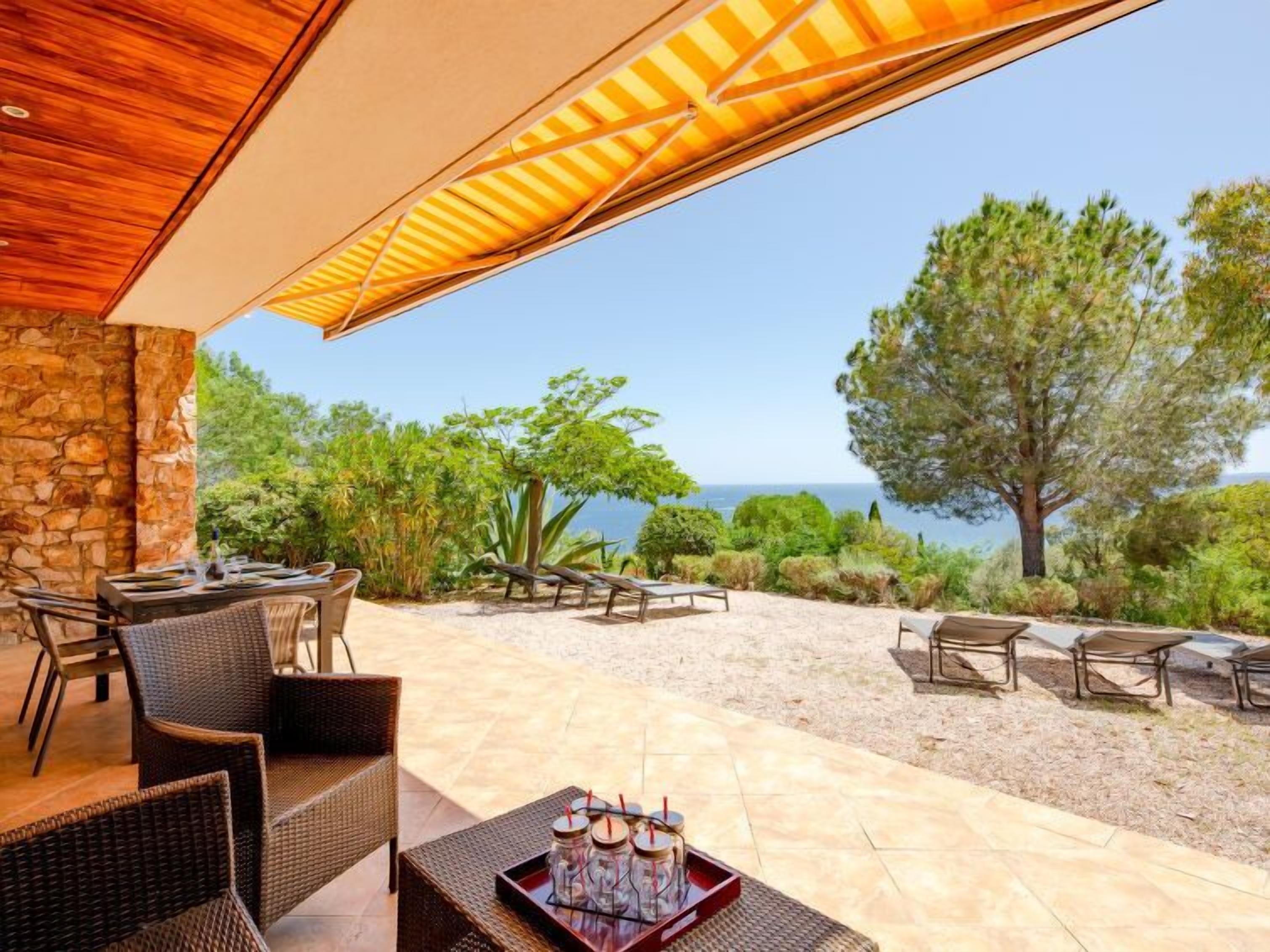 Patio esterno con mobili in vimini, muro in pietra e vista sul mare.